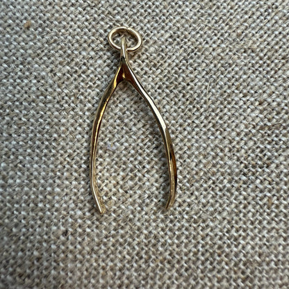 Gold wishbone pendant on a textured beige fabric background